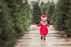 Young girl in red marches through rows of Christmas trees